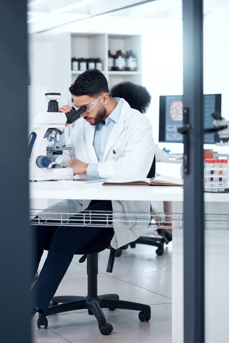 Microscope, man and analysis in laboratory for science, research and ppe for investigation. Technology, review and dna or data for healthcare with scientist and development for pharmaceutical company.