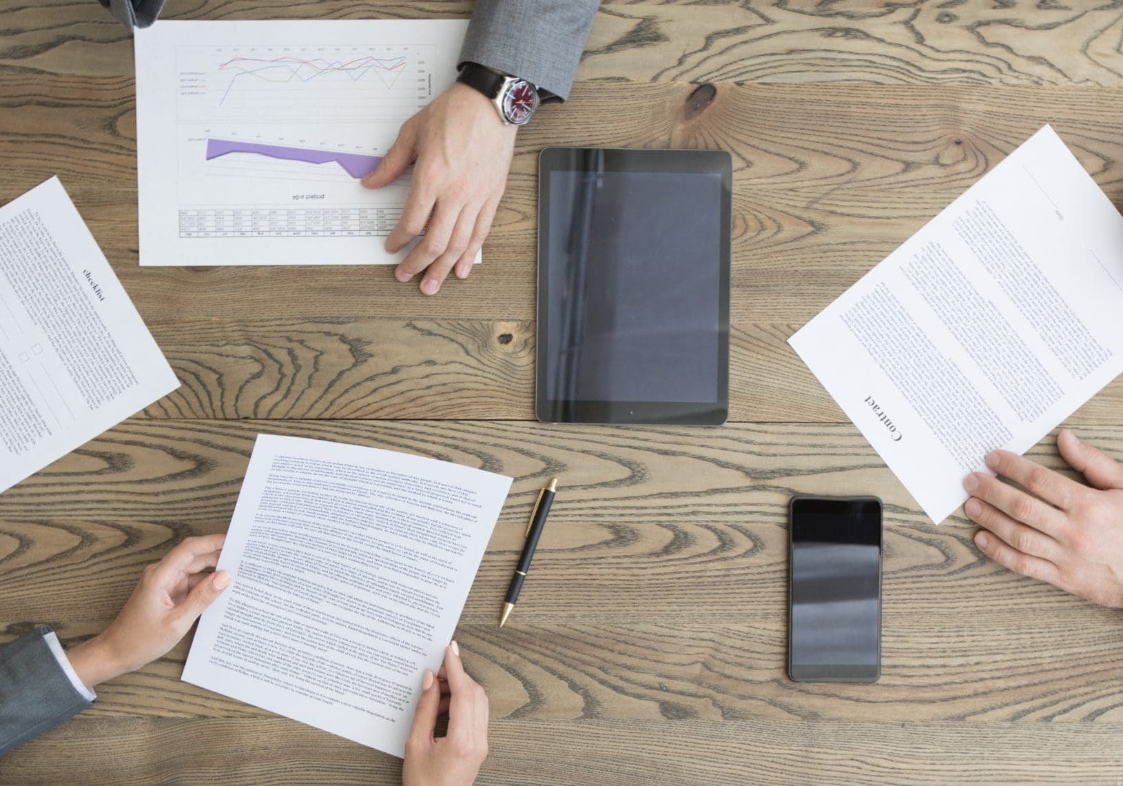 Business people discuss contract sitting around office table, top view